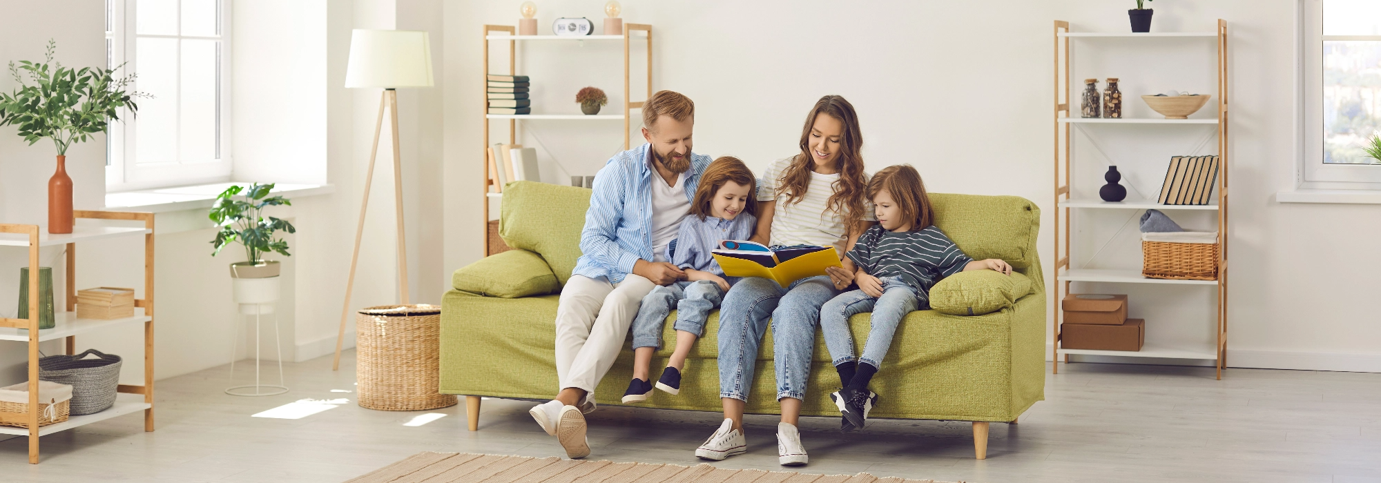 Eine Familie sitzt auf einem grünen Sofa und blättert gemeinsam durch ein Buch