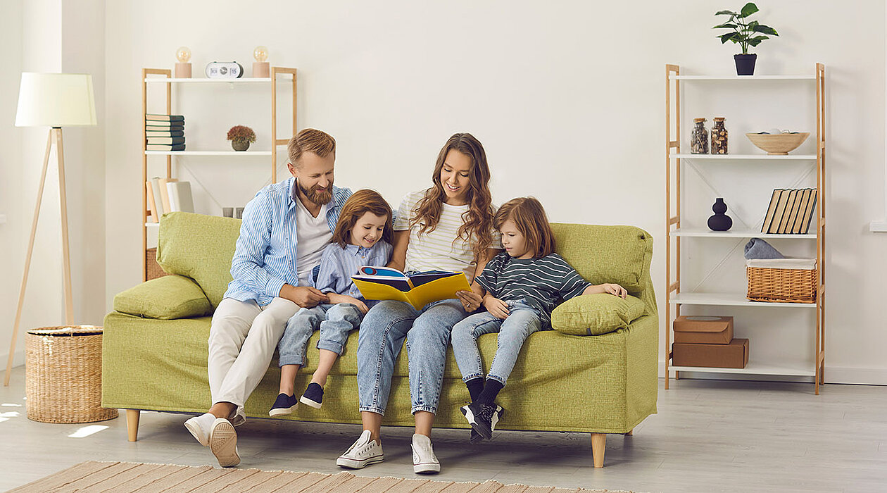 Eine Familie sitzt auf einem grünen Sofa und blättert gemeinsam durch ein Buch