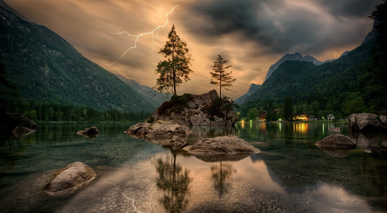 Ein düsteres Bild von einem See mit einer Felseninsel in der Mitte mit 2 Nadelbäumen darauf. Im Hintergrund gewittert es.